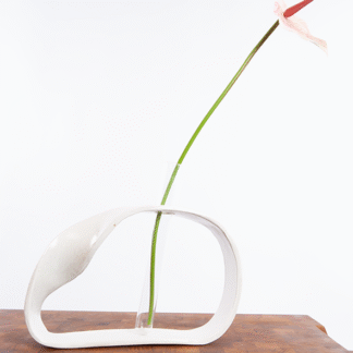 Håndlavet keramisk vase i organisk form med et klart reagensglas og en lang stilk med lys rosa blomst.