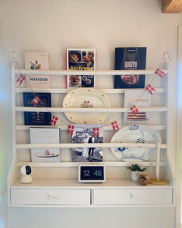 Porcelæns-flagranke med 10 røde og hvide flag hængt på en hylde sammen med bøger, fade og små dekorationer.